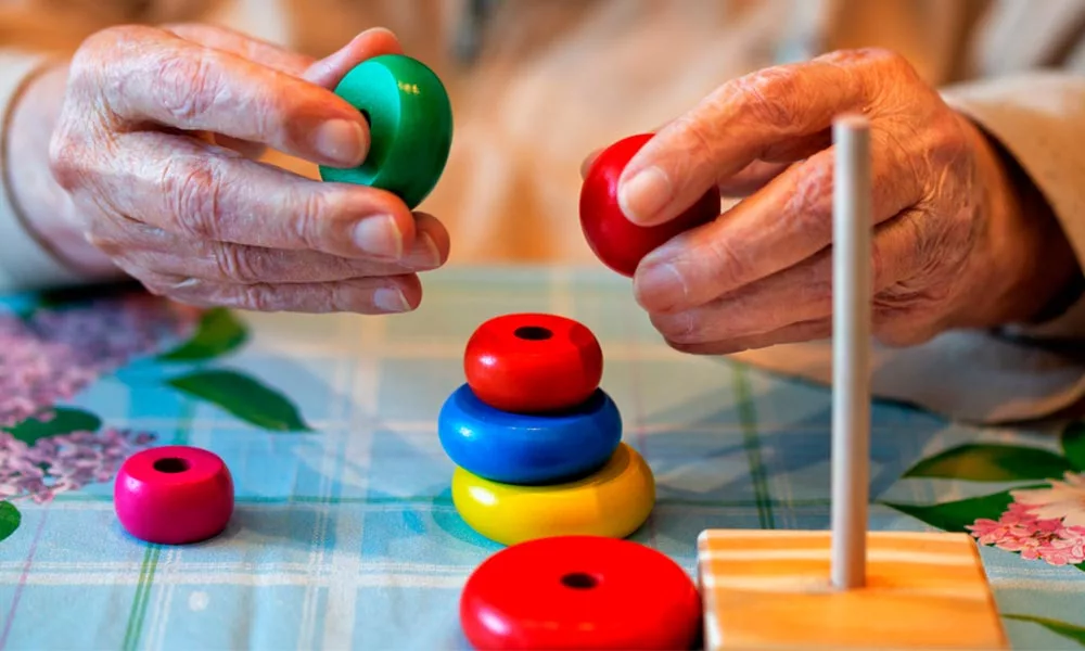 Manos de una persona mayor colocando piezas de colores como parte de una actividad cognitiva y motriz adaptada.
