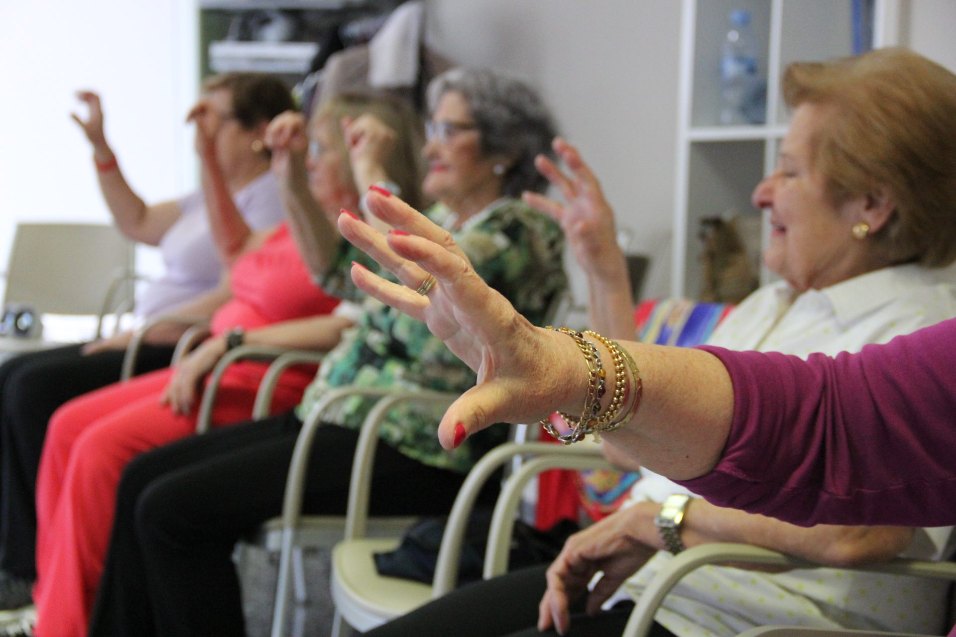 Mujeres mayores sentadas realizando ejercicios físicos adaptados en grupo dentro de una residencia geriátrica.