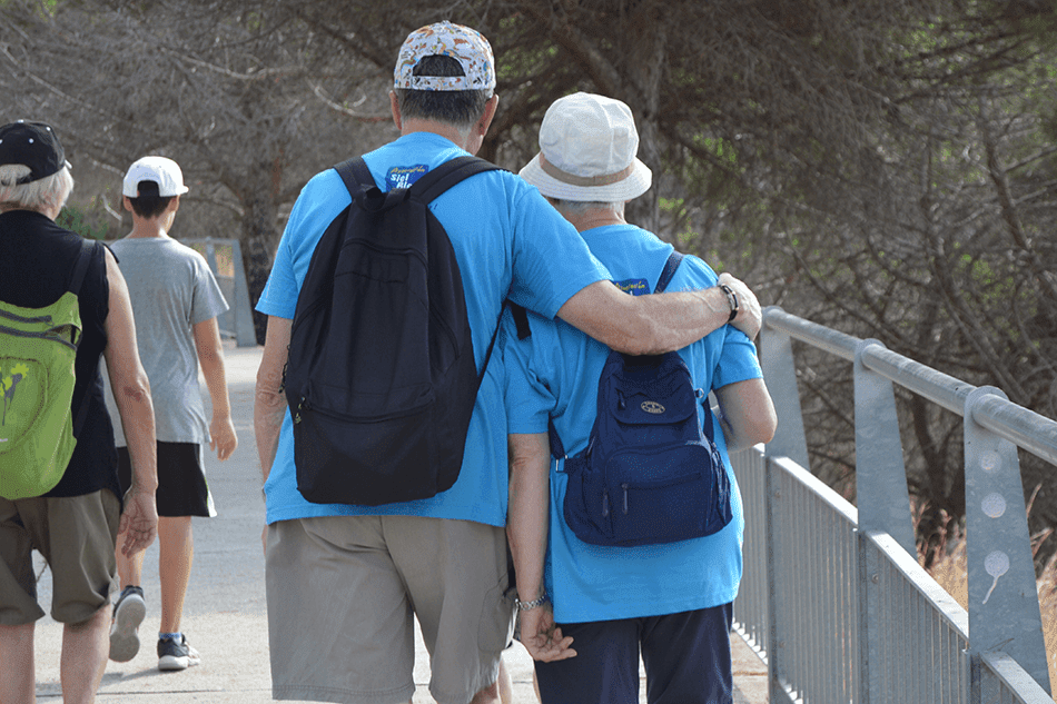 Dos personas mayores caminando abrazadas con mochilas azules durante una actividad de ejercicio al aire libre de la Fundación Siel Bleu.