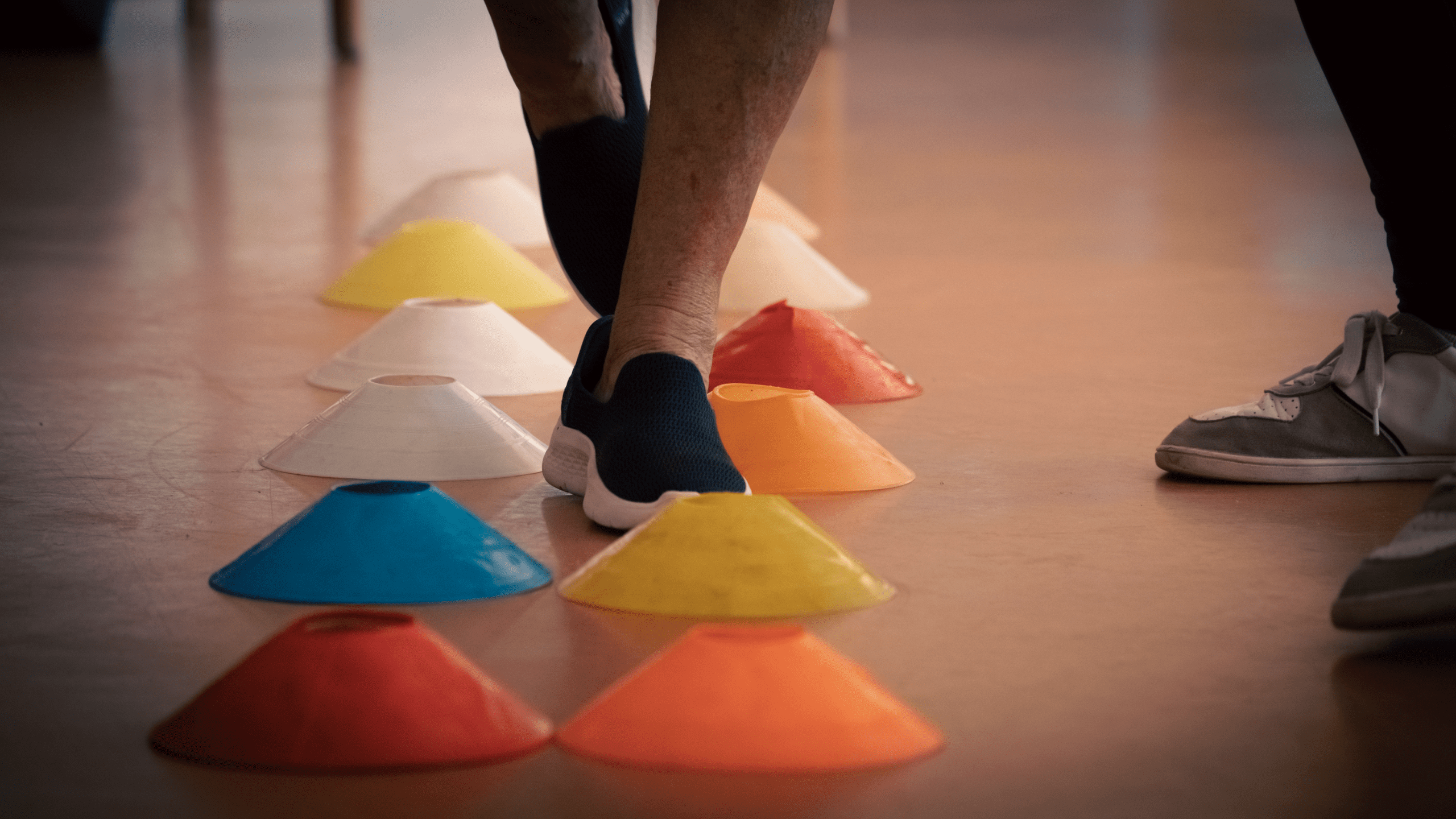 Persona mayor realizando ejercicio físico adaptado con conos de colores para mejorar el equilibrio, supervisada por un profesional de Fundación Siel Bleu