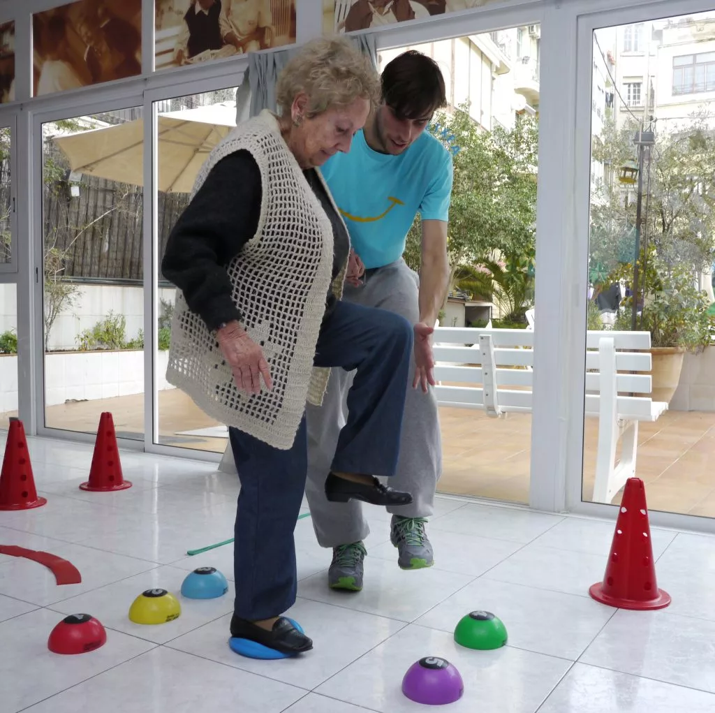 Mujer mayor haciendo ejercicio de equilibrio con supervisión de un entrenador de Siel Bleu
