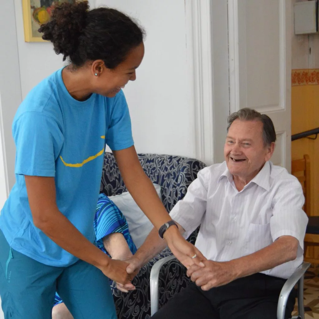 Entrenadora ayudando a un hombre mayor en silla a realizar ejercicios físicos adaptados