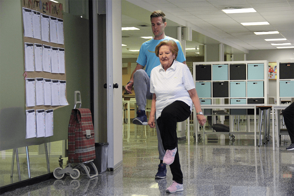 Mujer mayor con fibrosis pulmonar realizando ejercicio físico adaptado con la guía de un entrenador de Siel Bleu en una residencia o centro asistencial.