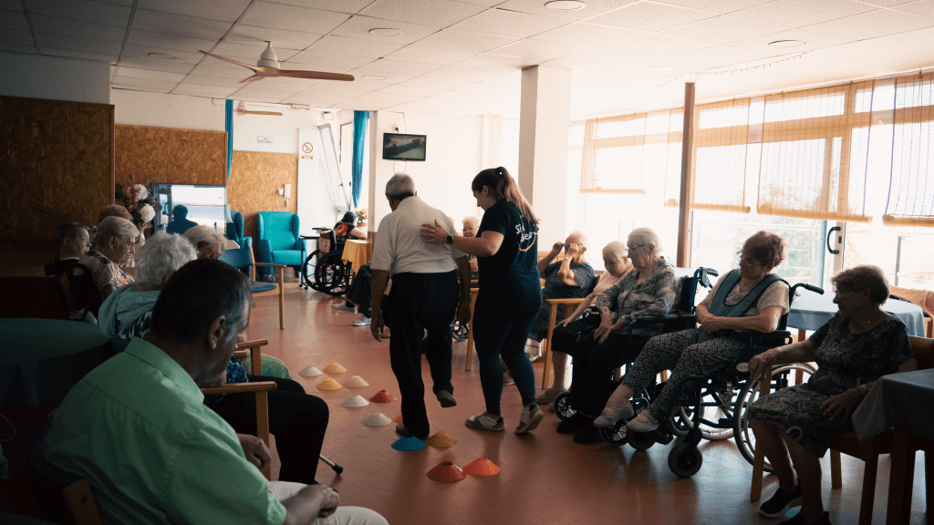 Técnica de Siel Bleu acompañando a una persona mayor durante una sesión de equilibrio en un circuito de ejercicio adaptado.
