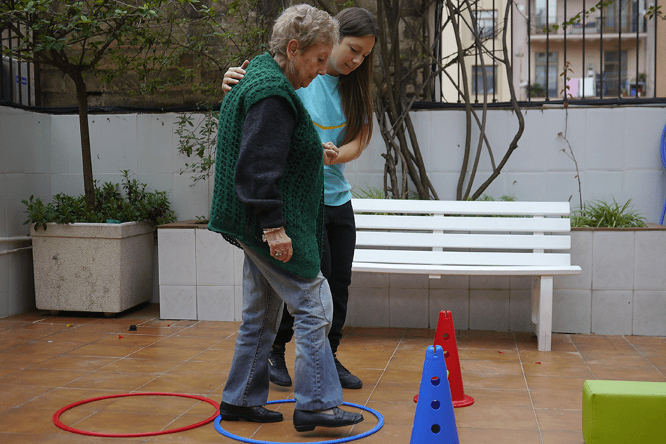 Persona mayor realizando ejercicios de movilidad con acompañamiento profesional en un entorno al aire libre. Actividad física adaptada para adultos mayores con apoyo personalizado.